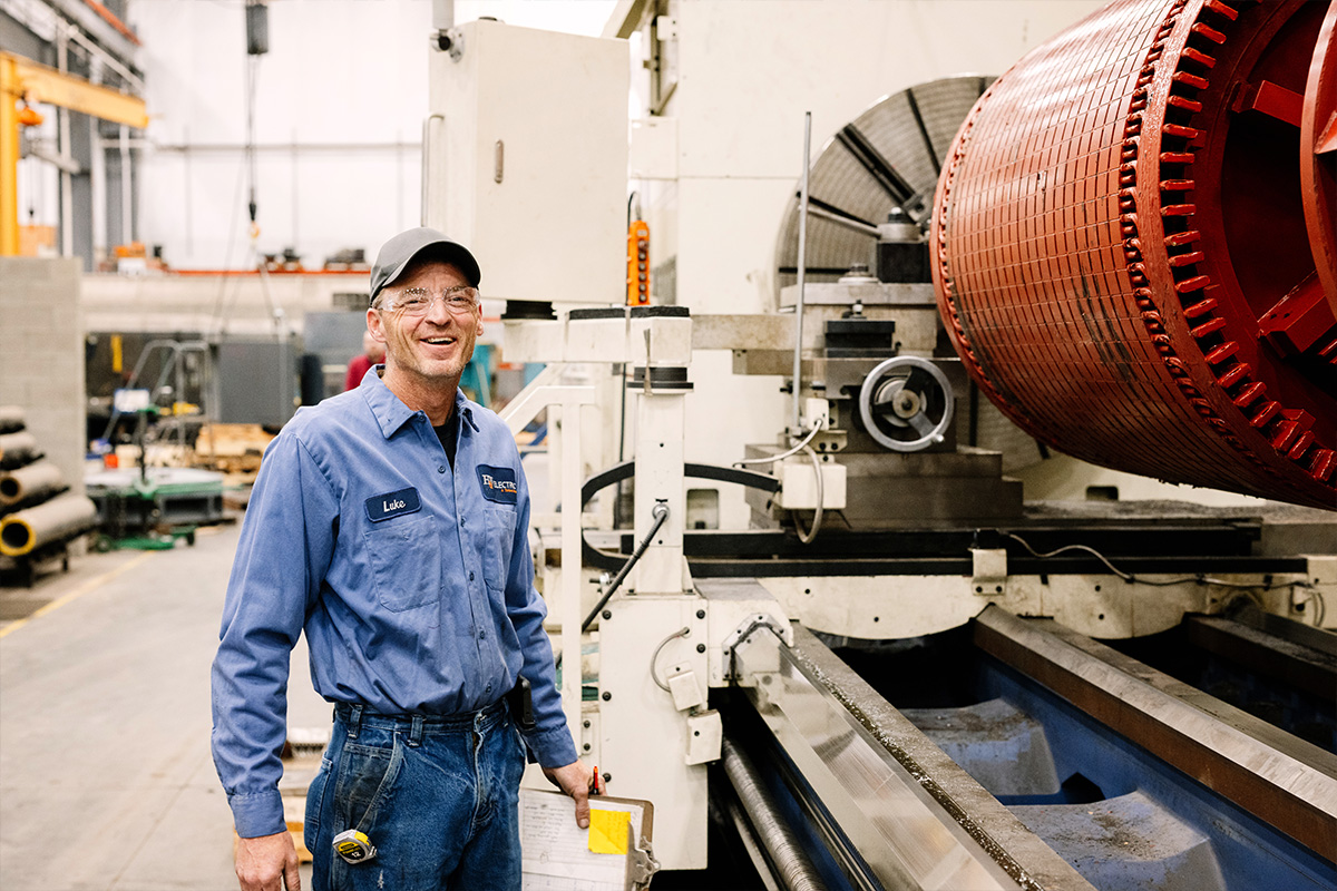 H&N Electrical industrial technician smiling while standing next to a comprehensive maintenance machine in their full-equipped facility