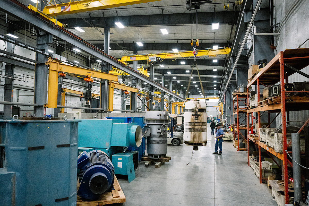 Wide angle shot of inside the full equipped H&N Electric facility as a person observes a machine part being suspended by an indoor crane