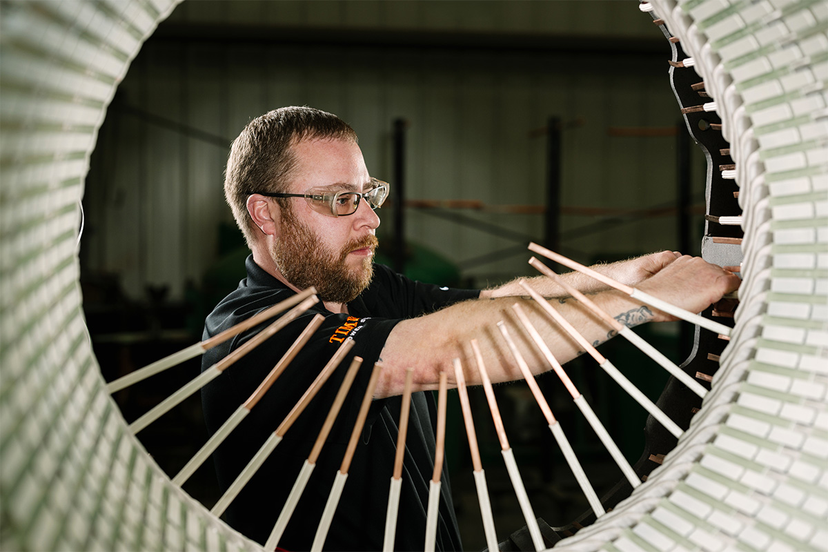 H&N Electric technician framed by an industrial motor generator with coils sticking up as they wind the generator